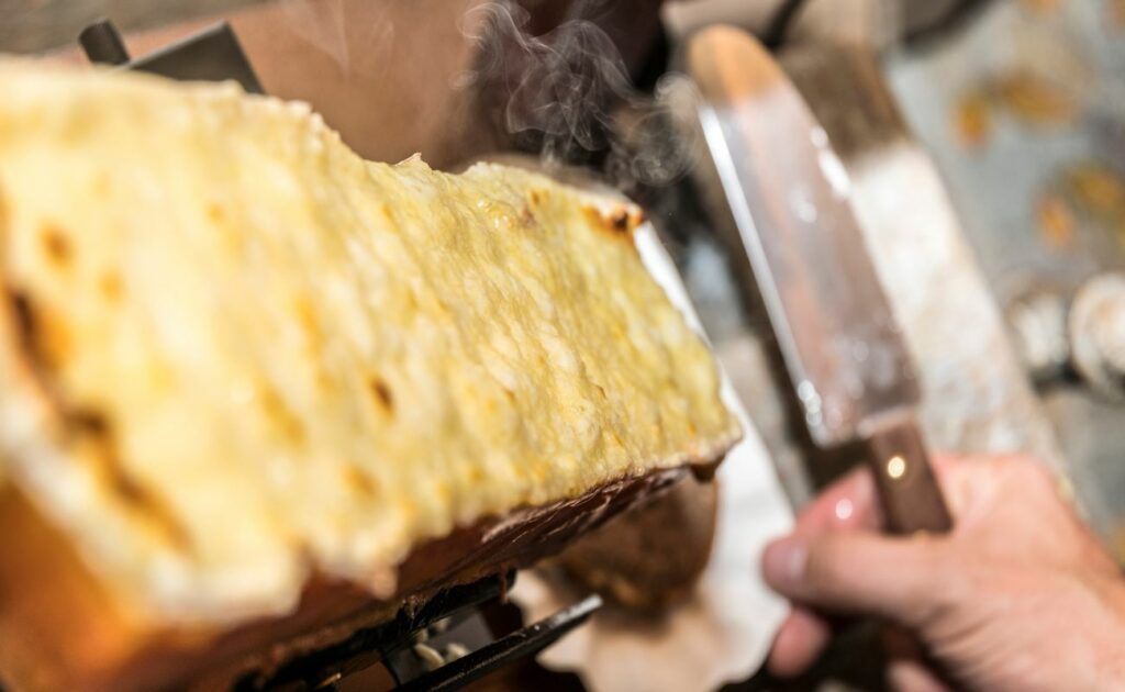 Geschmolzener Raclette-Käse wird mit einem Messer abgeschabt
