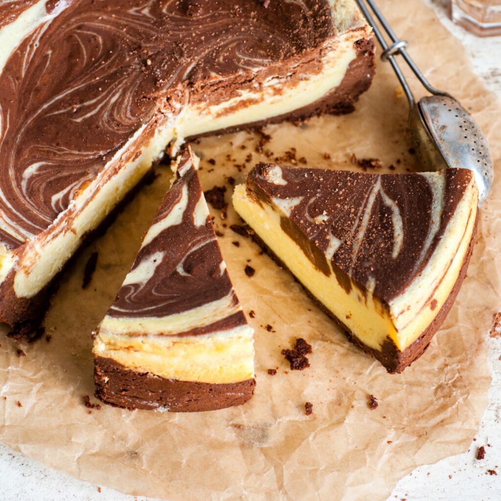 Marmor-Käsekuchen wird angeschnitten auf Backpapier präsentiert.