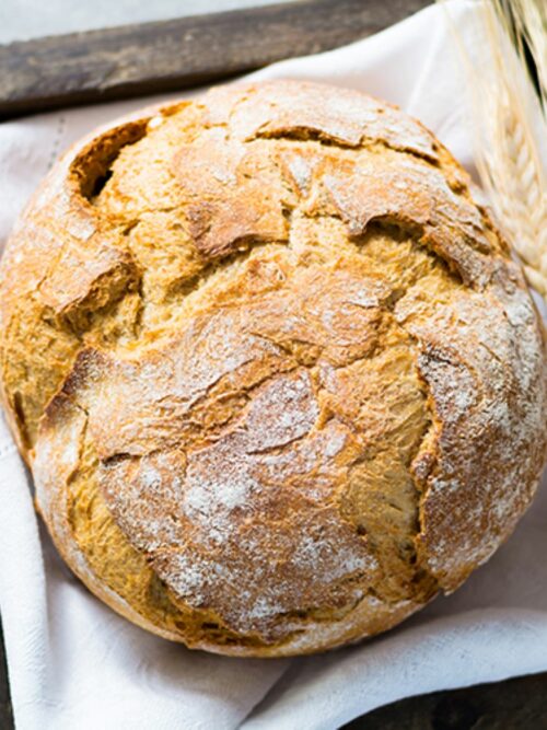 Weizenbrot wird von oben auf einem weißen Tuch gezeigt und mit Weizen dekoriert gezeigt.