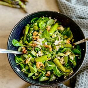 Grüner Spargel-Salat wird in einer dunklen Schüssel mit Salat-Besteck gezeit