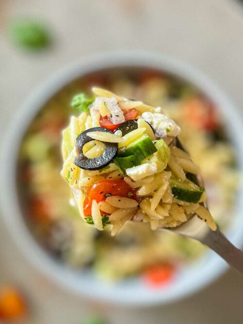 Kritharaki-Salat wird auf einem Löffel vor unscharfer Schüssel gezeigt.
