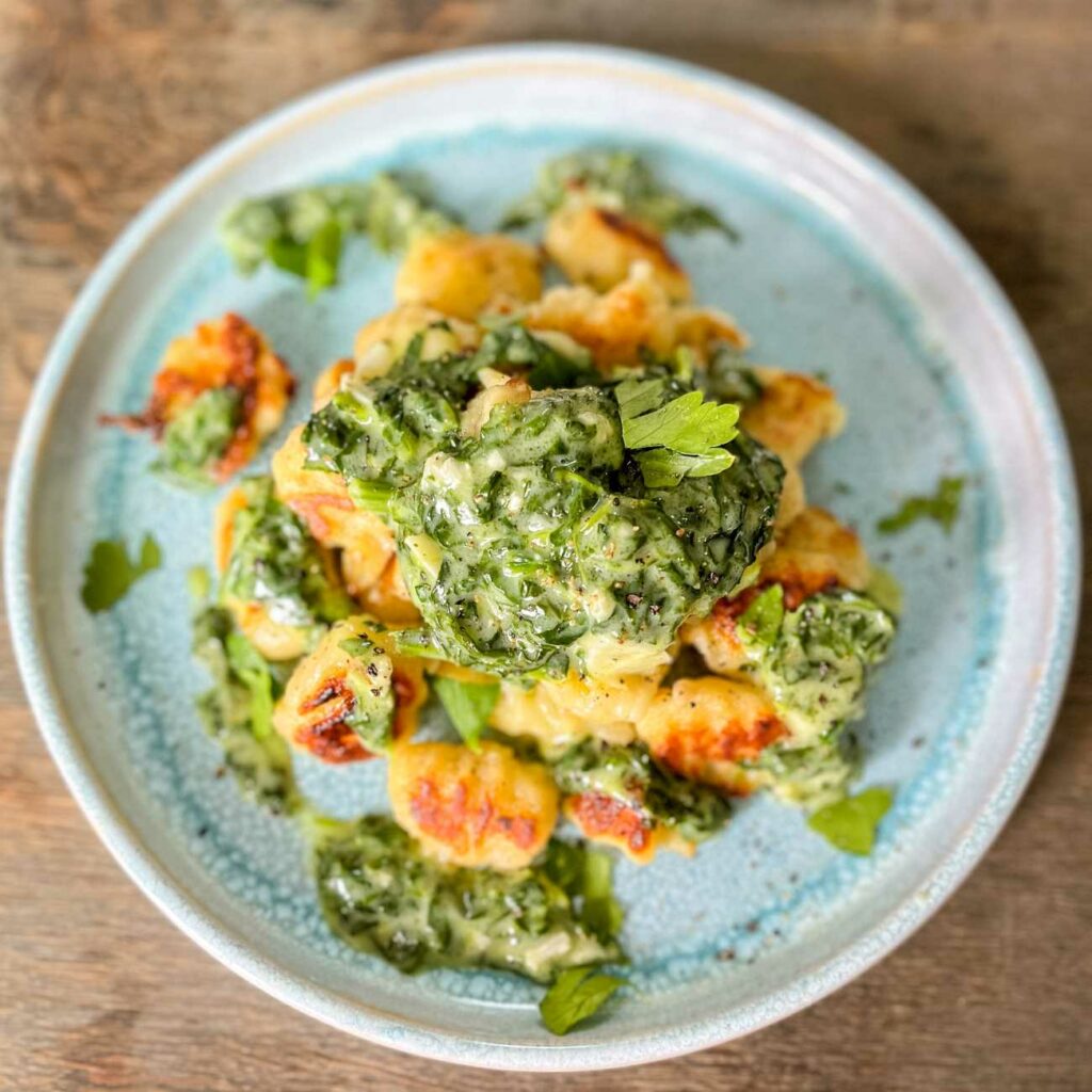 Gnocchi ve špenátu a omáčce gorgonzola jsou zobrazeny shora na modrém talíři.