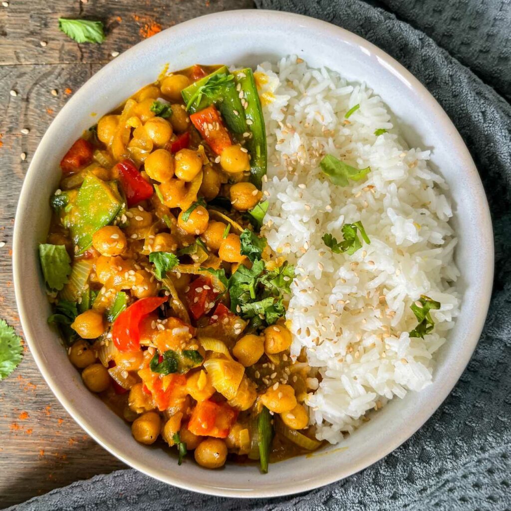 Čičerikin curry postrežemo z rižem v skledi, posut s sezamovimi semeni in koriandrom.