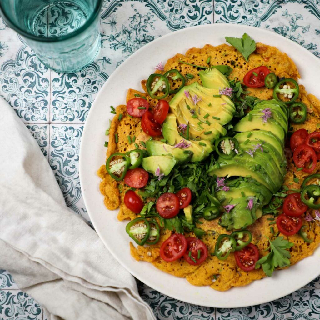Veganska omleta je prikazana s solato in avokadom na krožniku na pisanih ploščicah.