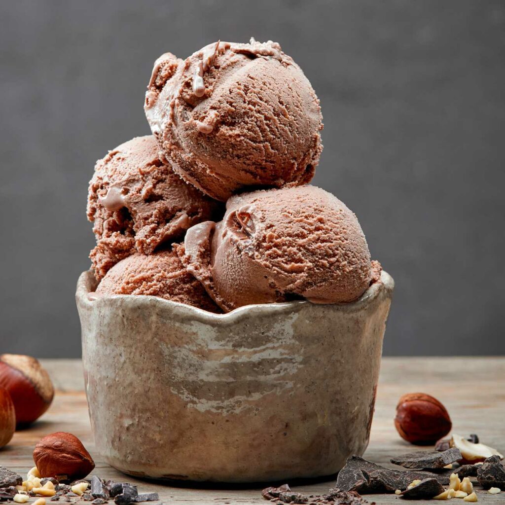 Lieskovooriešková zmrzlina je zobrazená v miske s lieskovými orieškami a trochou čokolády.