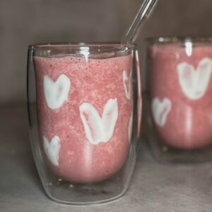 Smoothie mit Joghurt-Herzen wird in zwei doppelwandigen Gläsern mit Glas-Strohhalm gezeigt.