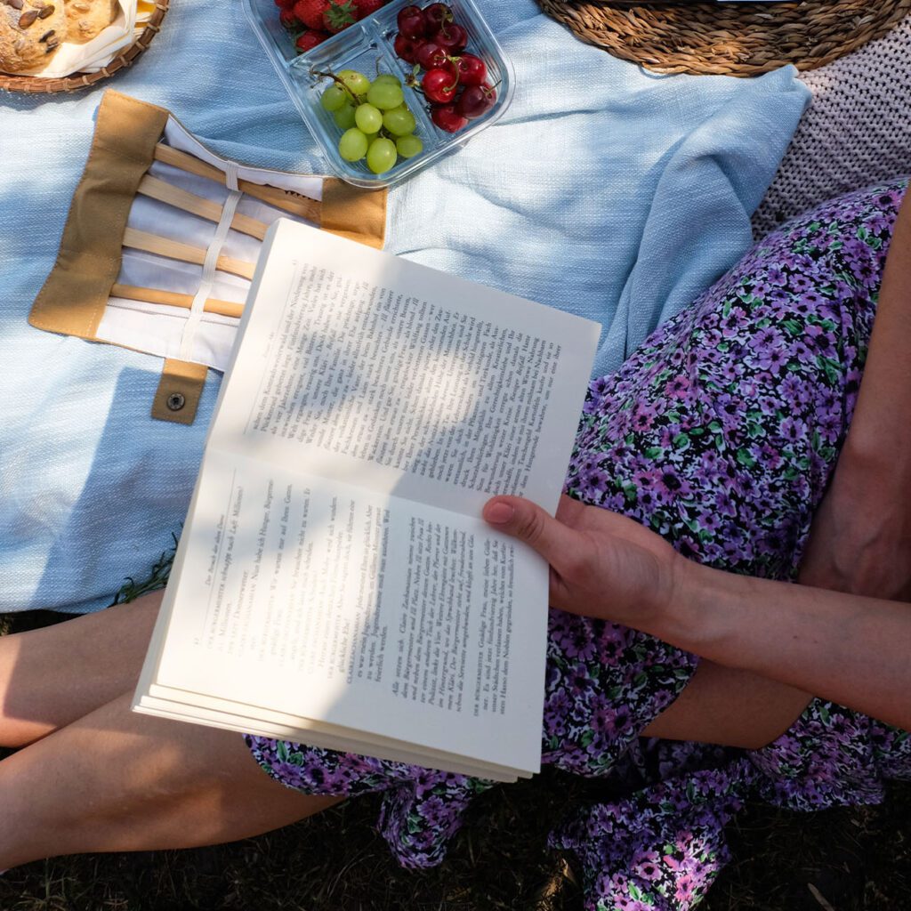 Picknick Rezepte: Ein Buch wird auf einer Picknick Decke in der Sonne gelesen.