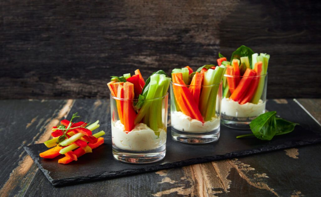 Zdravé občerstvenie: Zeleninové tyčinky sú zobrazené v nádobe s dipom na dne.