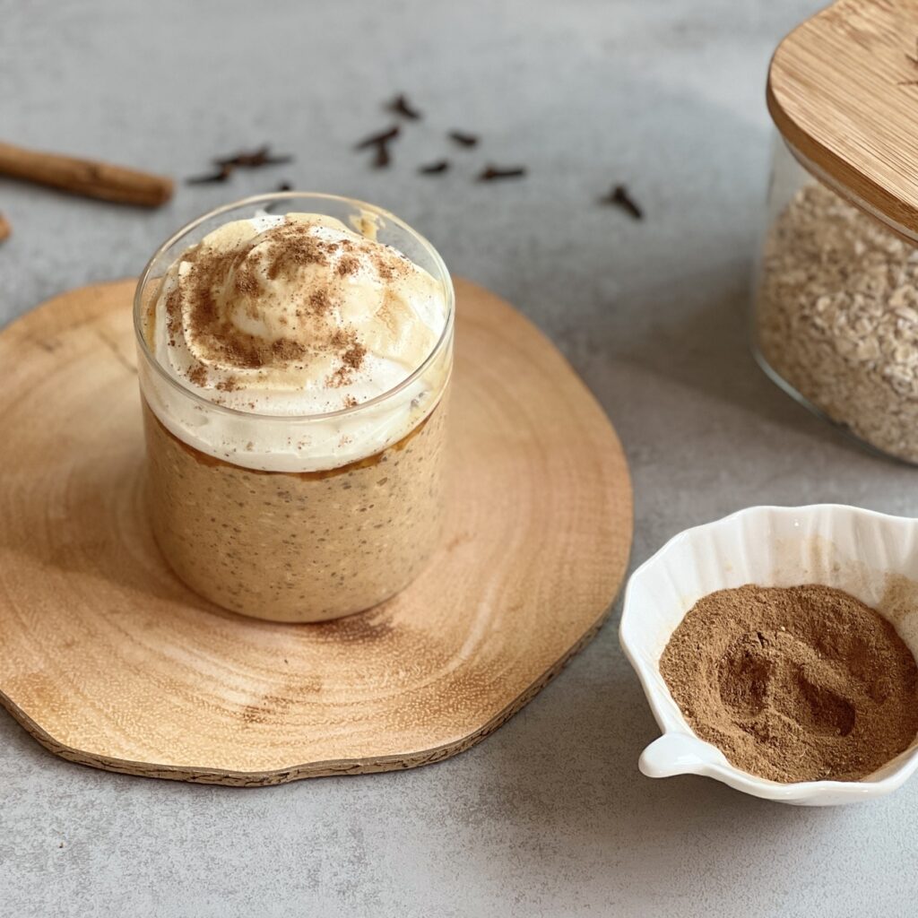 Kürbis Overnight Oats werden in einem Glasgefäß mit Schlagsahne und Ahornsirup serviert.