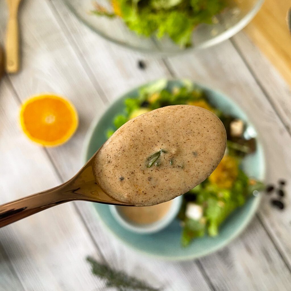 Orangen-Zimt-Dressing wird auf einem goldenen Löffel über einem Salat gezeigt.