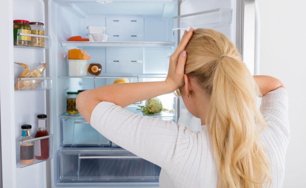 Geruch im Kühlschrank: Frau steht ratlos vor ihrem Kühlschrank.